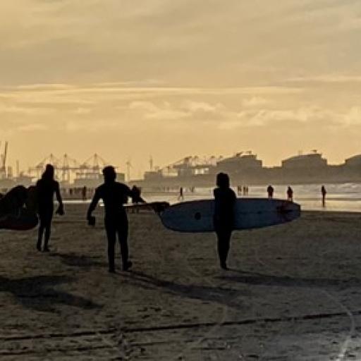 sunset picture of a beach with people carrying their boards
